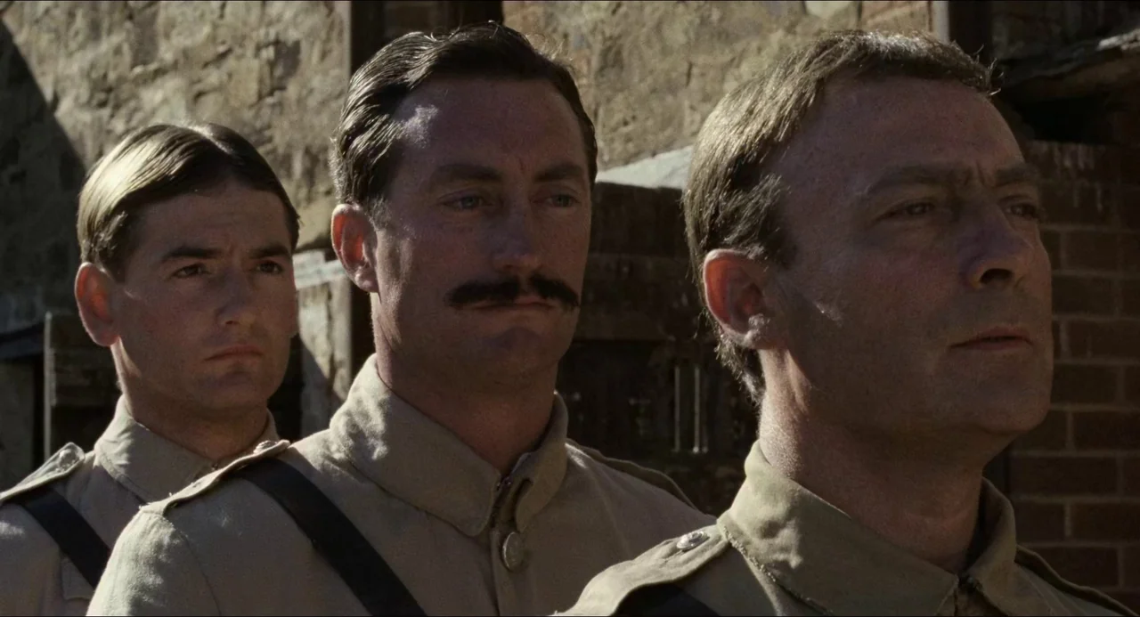 Breaker Morant (1980) movie still: medium — Three soldiers in tan uniforms stand aligned against a rough brick wall exterior. They look forward with…