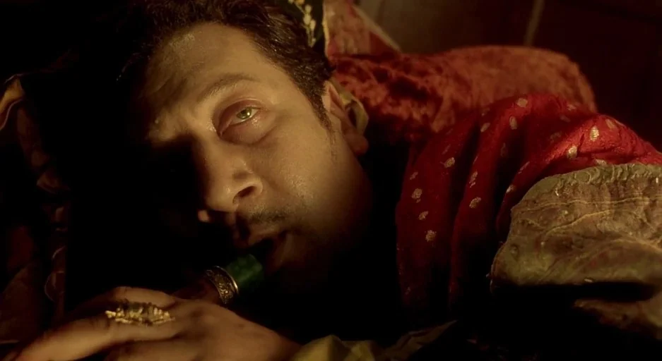 The City Of Lost Children movie still: closeup — A dimly lit, cramped interior space draped with heavy red fabric and decorative textiles. A man…