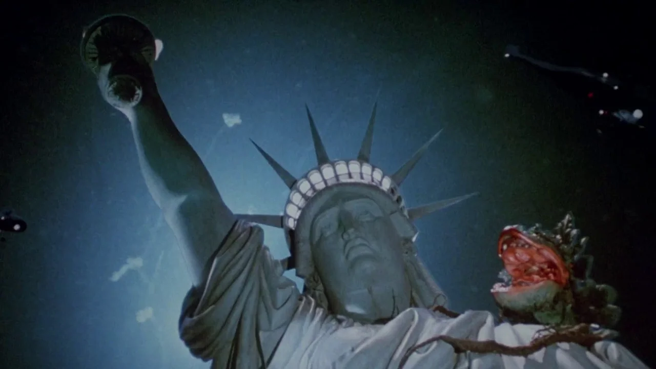 Little Shop of Horrors (1986) movie still: medium — The iconic Statue of Liberty head is illuminated at night against a dark backdrop. A small,…