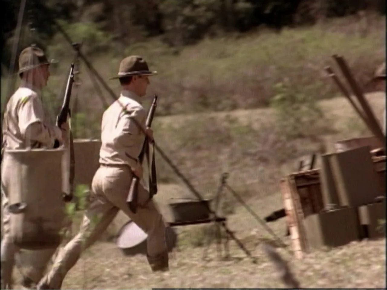 In Pursuit of Honor (1995) movie still: fullbody — Two soldiers run through an open field on a sunny day. They carry rifles and wear tan military…