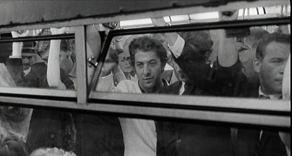 Midnight Cowboy (1969) movie still: medium — A crowded interior of a vintage city bus with passengers standing in transit. A man stands at the…