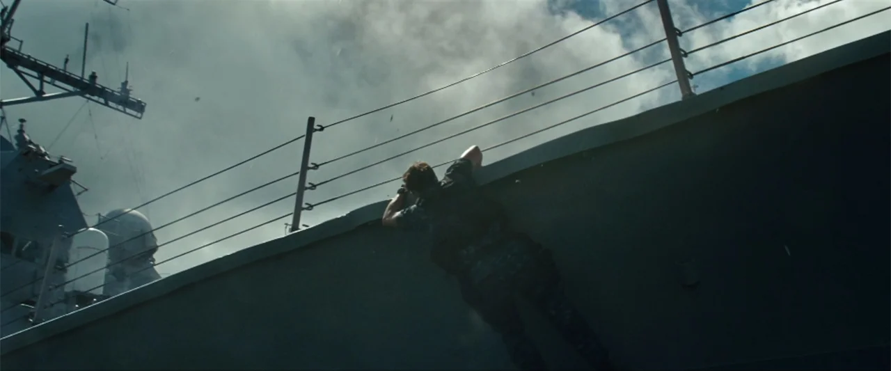 Battleship (2012) movie still: wide — A naval vessel exterior with metal railings against a bright sky with heavy clouds. A man in tactical gear…