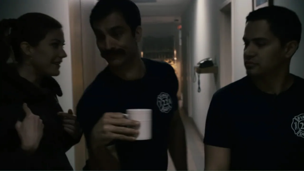 Quarantine (2008) movie still: medium — A sterile medical hallway with plain walls and a wall-mounted telephone terminal. Three people stand…