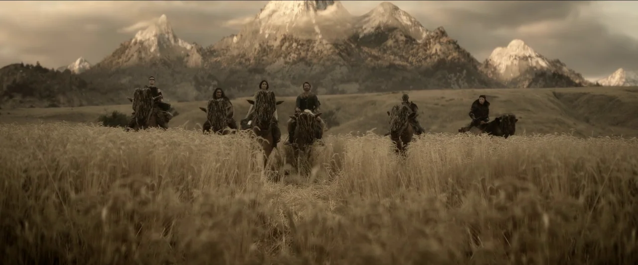 Rebel Moon – Part One: A Child of Fire (2023) movie still: wide — A group of riders traverses a sprawling field of tall dry grass. Sharp mountain…