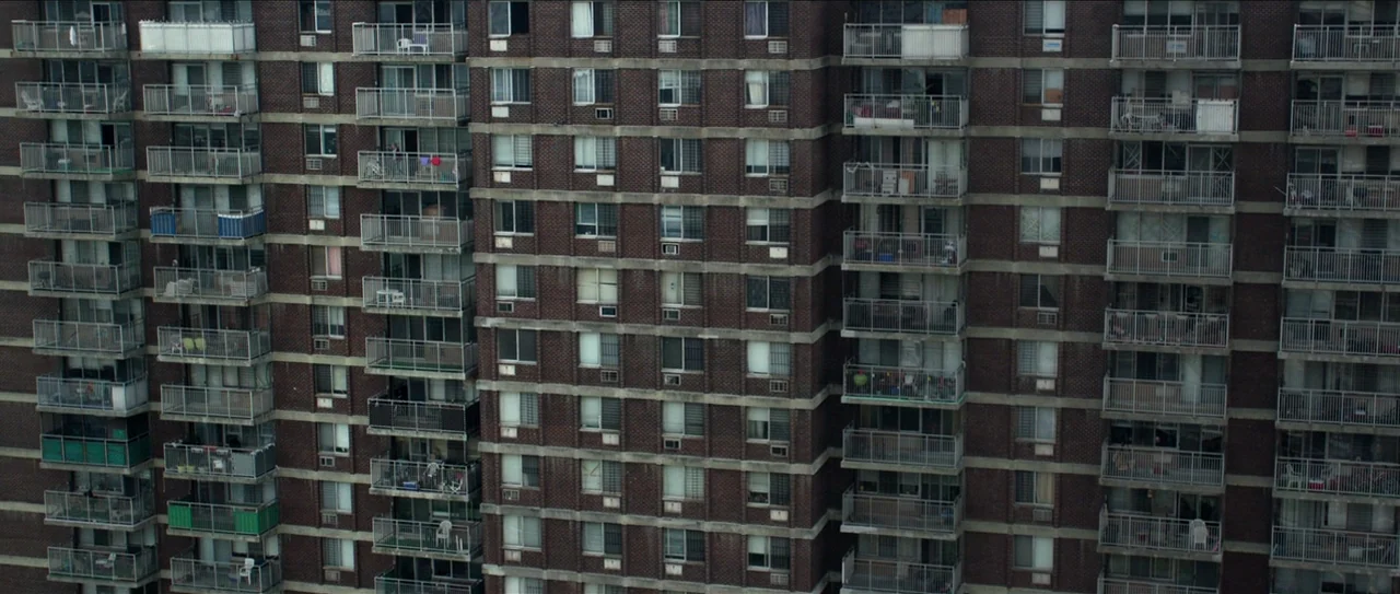 Nerve (2016) movie still: establishing — A dense urban brick residential high-rise features repetitive balconies and windows across its facade.…