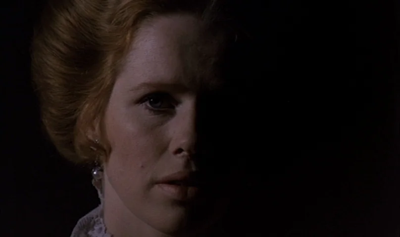 Cries and Whispers (1972) movie still: closeup — A woman stands in a dark environment with light falling only on half her face. She looks slightly…