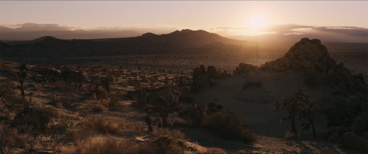 Woman of the Hour (2024) movie still: establishing — A vast desert expanse under a bright setting sun with rocky outcrops and vegetation. The…