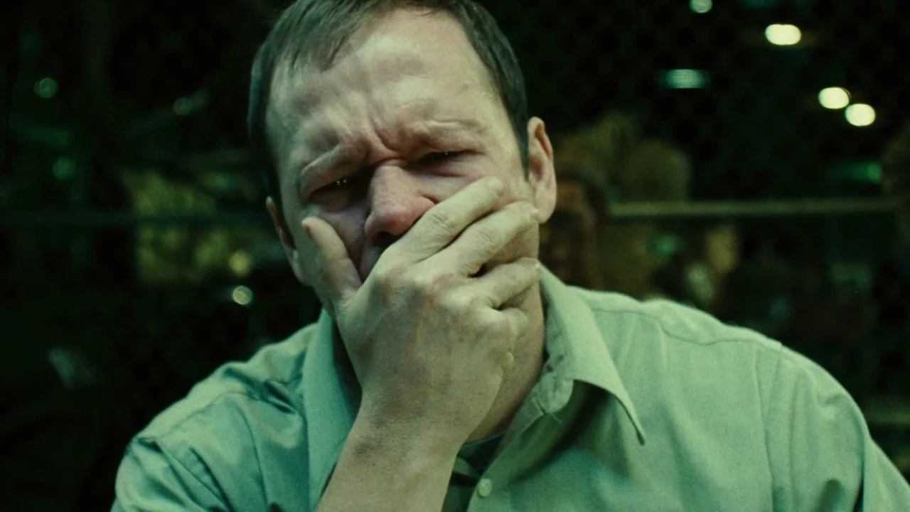 Saw II movie still: closeup — A dimly lit office space featuring a green-toned industrial environment with out-of-focus background details. A…