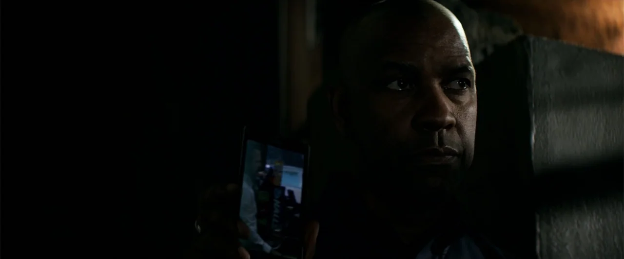 The Equalizer (2014) movie still: closeup — A dark interior setting with the subject partially obscured by shadow. An older man holds a glowing…
