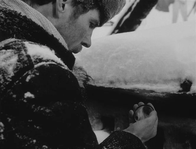 The Ascent (1977) movie still: closeup — A snow-covered outdoor environment with thick drifts of white snow on a wooden structure. A man in a dark…