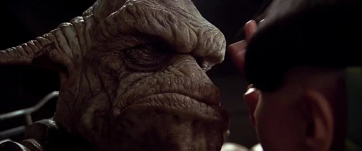 The Fifth Element (1997) movie still: closeup — A dark laboratory setting frames a close encounter between a human and an alien. A human hand…