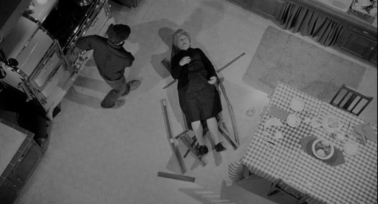 Psycho III (1986) movie still: wide — A high-angle view shows a domestic kitchen with a checkerboard tablecloth. A woman lies in a broken wooden…