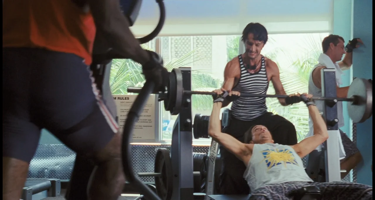 I Love You Phillip Morris (2010) movie still: medium — A brightly lit gym area features a weight bench near a large window. One man lies on the…
