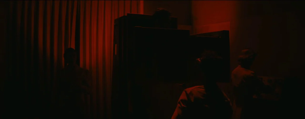 Bigger Than Life (1956) movie still: wide — A darkroom features heavy curtains and large technical equipment under a red glow. Several people occupy…