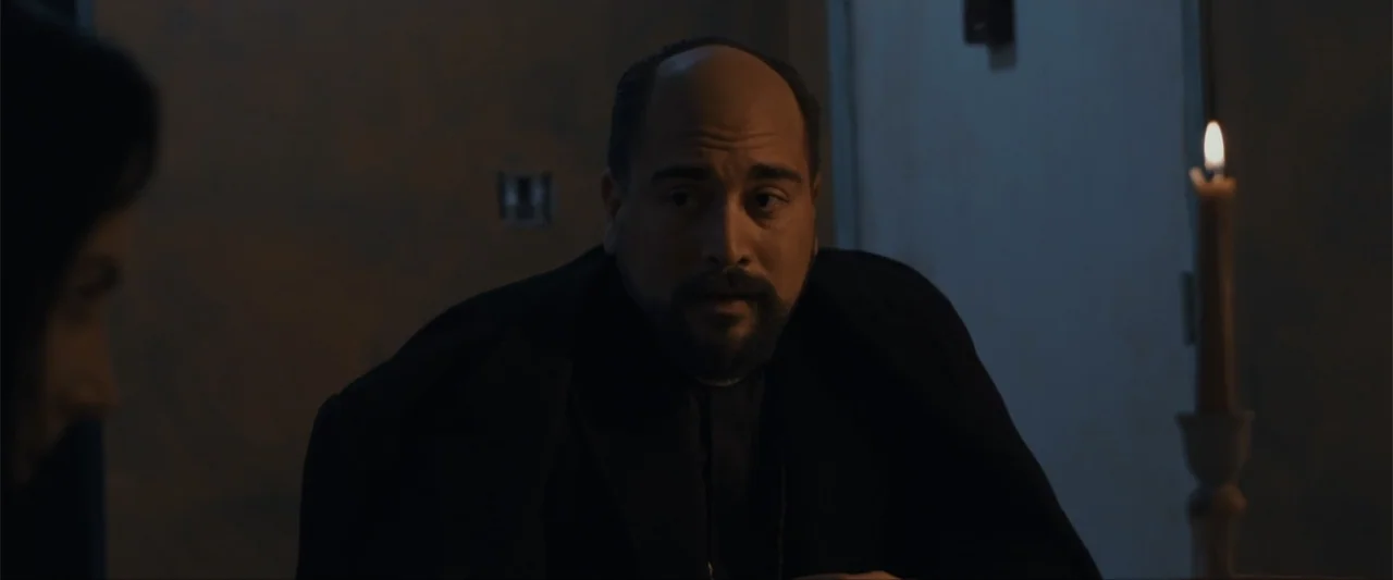 Anomaly (2006) movie still: medium — A dimly lit room with dark walls and a singular candle providing illumination. A man with a beard in a dark…