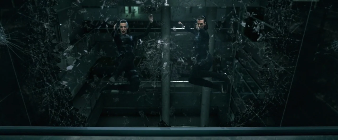 Resident Evil: Afterlife (2010) movie still: wide — A multi-story building atrium features glass railings and concrete pillars in the dark. Two…