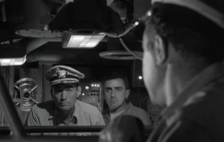 On The Beach (1959) movie still: medium — The interior of a military submarine features cramped, cluttered metal walls and machinery. Two officers…