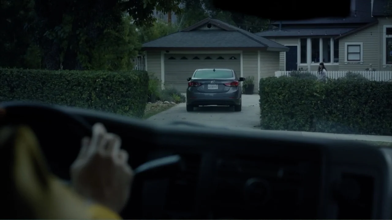 Storm Damage (2000) movie still: medium — A suburban residential street features a parked car in a driveway before a house. A person stands near a…