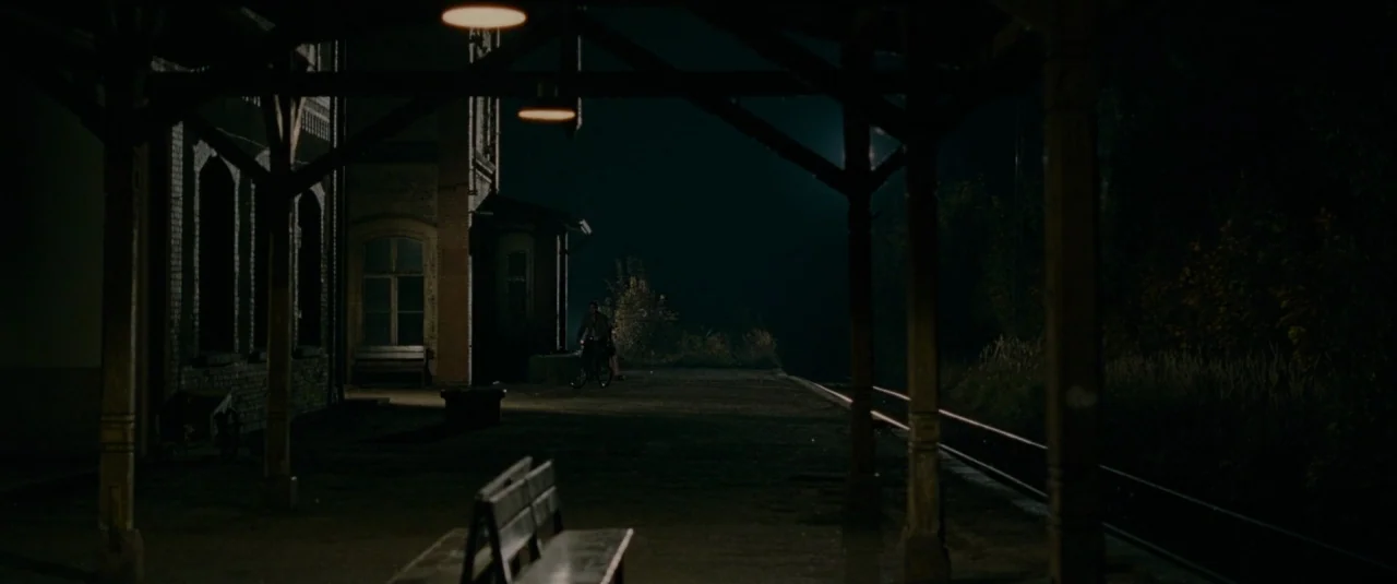 Phoenix (2014) movie still: wide — A night view of a deserted train station platform with a covered wooden structure. The concrete surface extends…