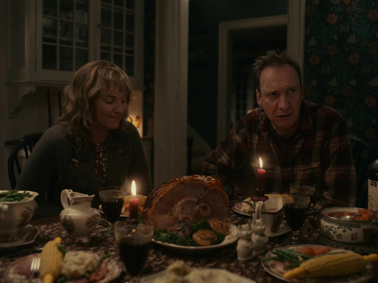 I’m Thinking of Ending Things (2020) movie still: medium — A dimly lit room with patterned wallpaper features a table set for a holiday dinner. A…