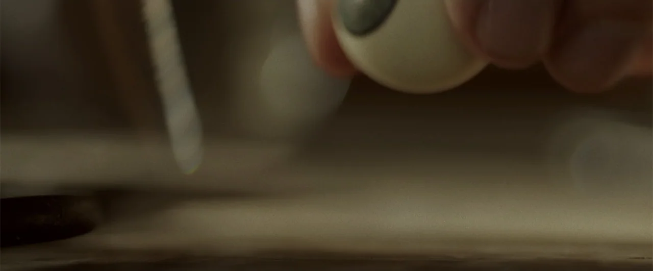 Annabelle: Creation (2017) movie still: closeup — A close view of a smooth surface in a dimly lit workshop environment. A person holds a small…
