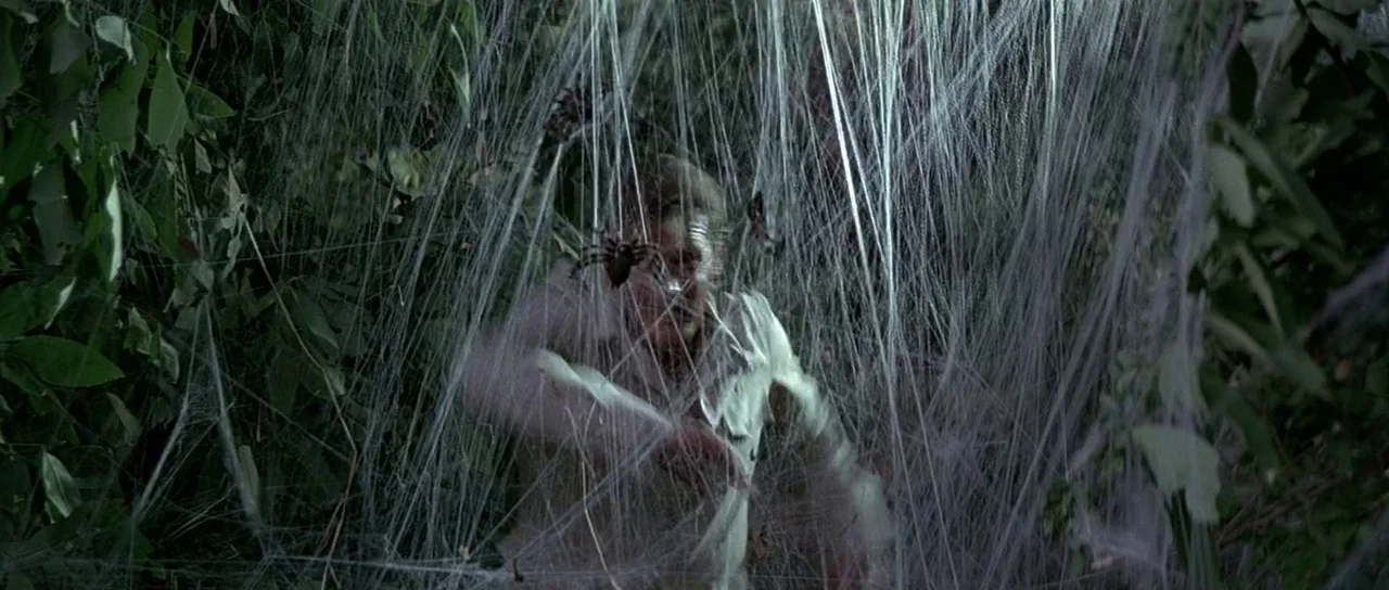 Octopussy (1983) movie still: medium — A man is caught amidst an intricate, layered expanse of thick white spider webs. He is pushing his arms…