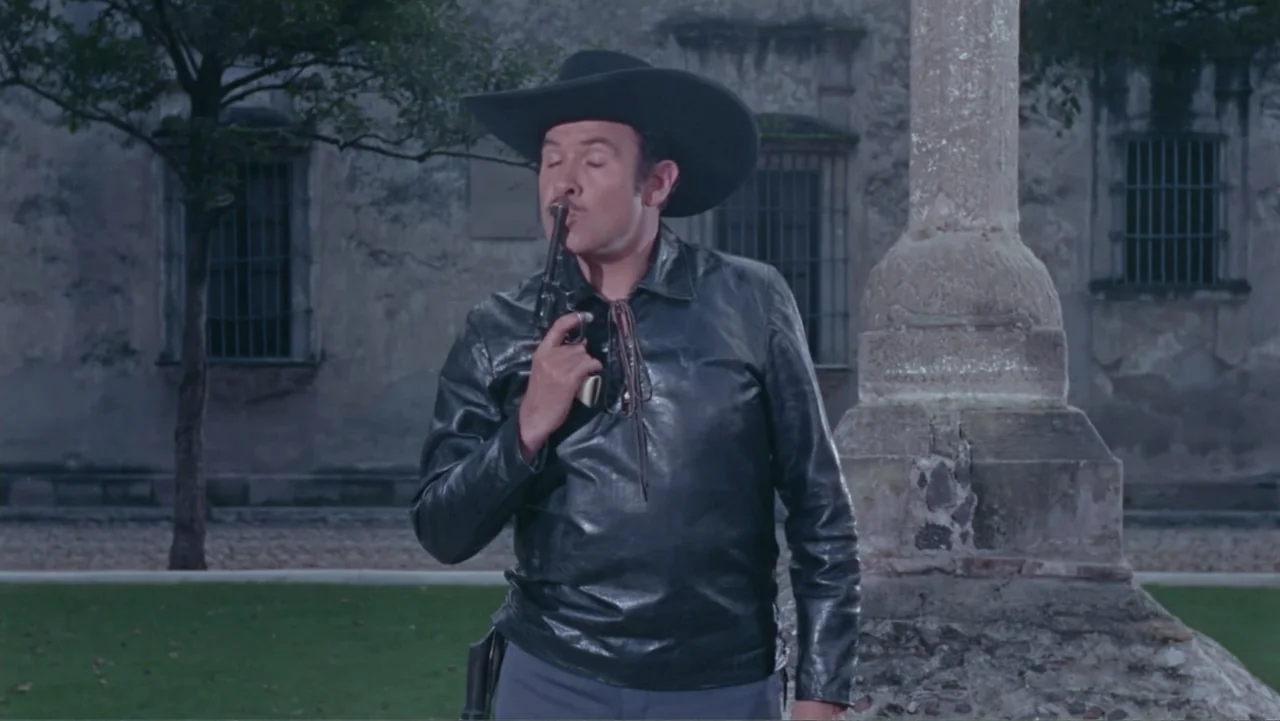 Los Dos Rivales (1966) movie still: medium — An stone-walled courtyard features an old stone cross monument in the background. A man in a black…