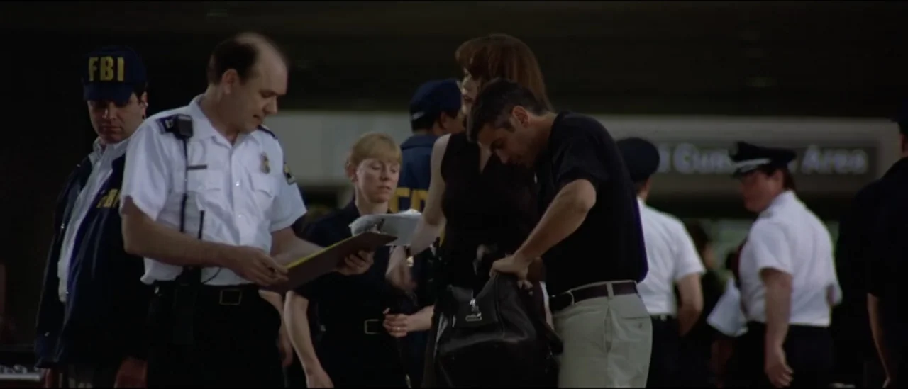 The Peacemaker (1997) movie still: medium — A group of law enforcement officers stand near a public terminal entrance area. A man in a dark polo…