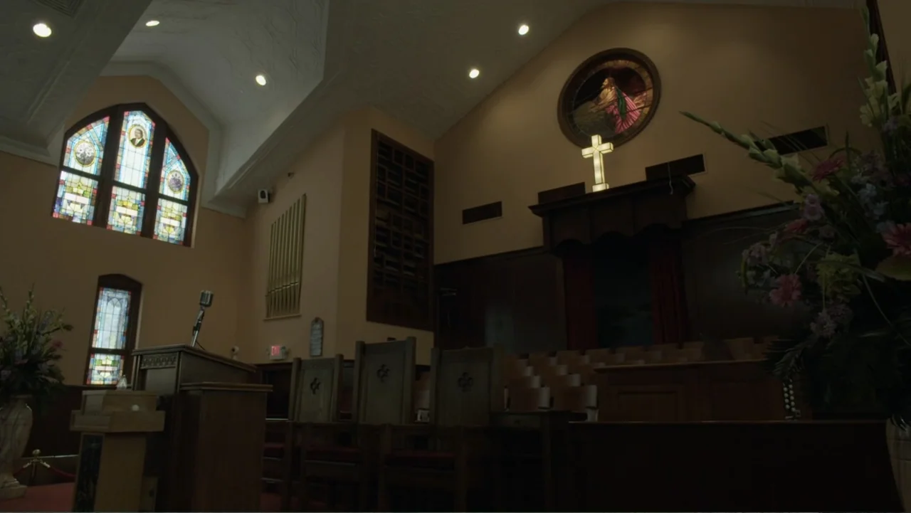 King in the Wilderness (2018) movie still: establishing — A church sanctuary features wooden pews, a pulpit with a microphone, and stained glass…
