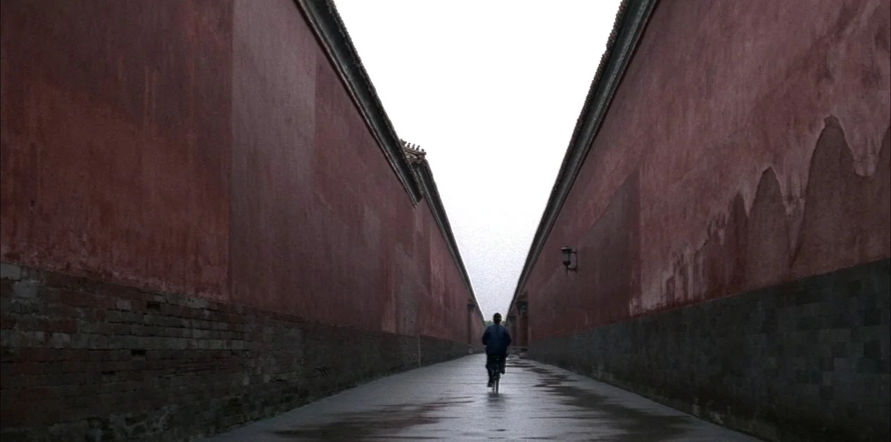 The Last Emperor (1987) movie still: wide — A narrow alleyway enclosed by high, weathered red stucco walls with grey stone bases. A single person…