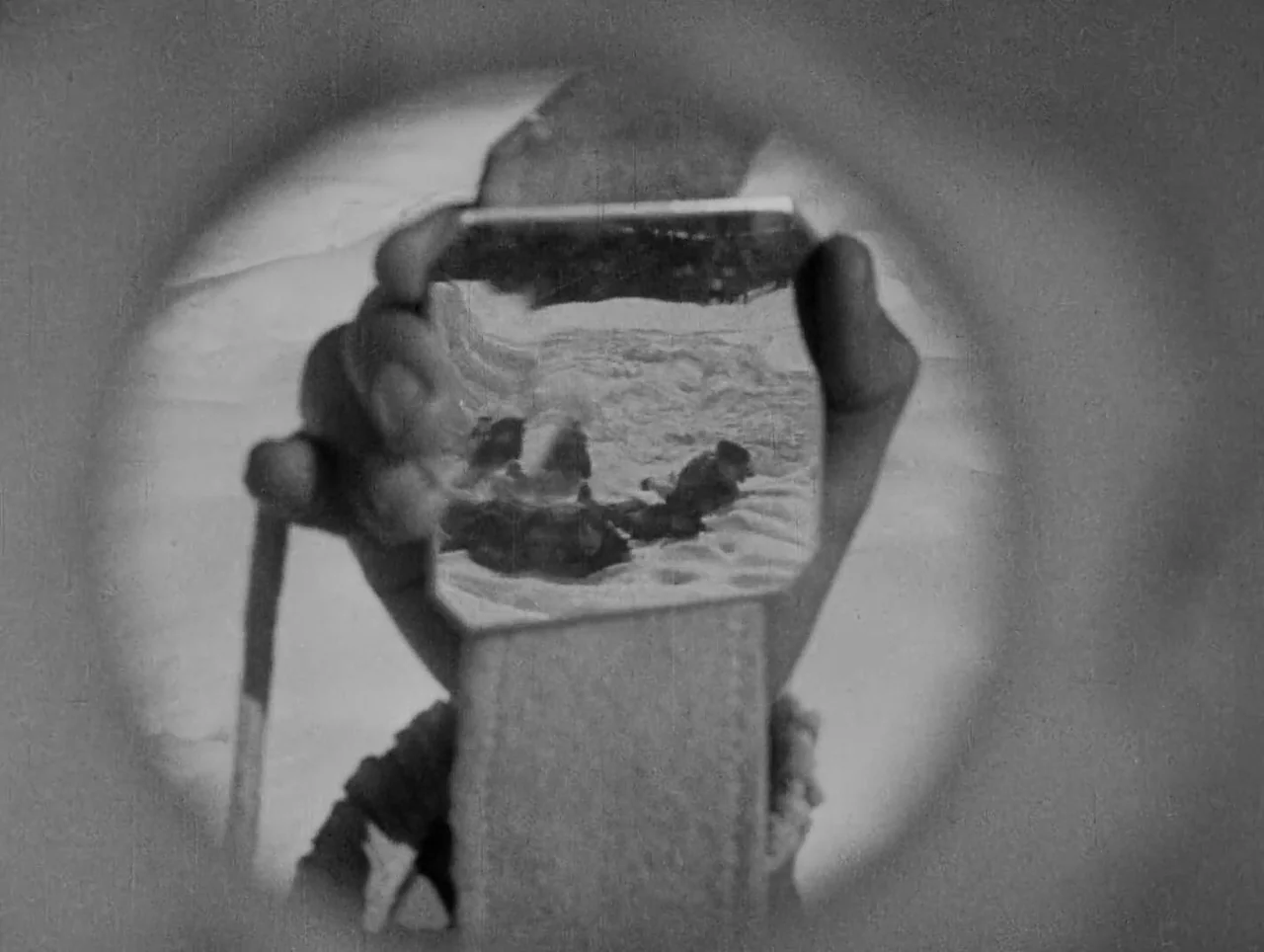 Napoleon (1927) movie still: closeup — A close-up view through a circular frame reveals a hand holding a small photograph. The photograph depicts…