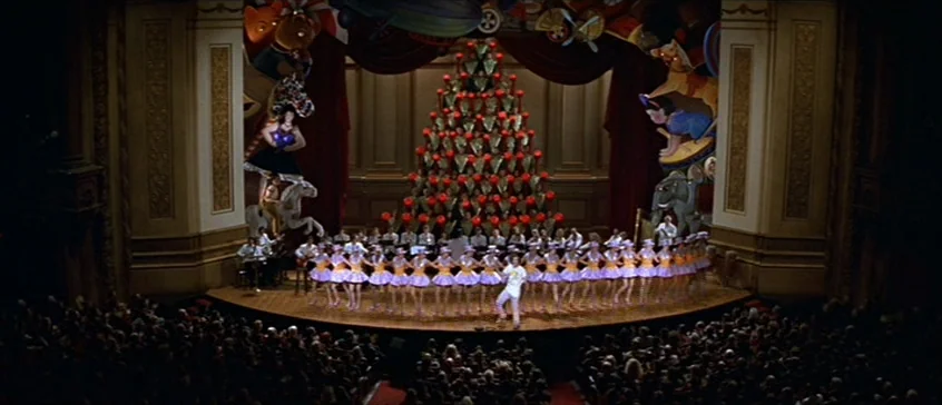 Man On The Moon (1999) movie still: wide — An ornate proscenium stage hosts a large chorus of dancers beneath a Christmas tree installation. A…