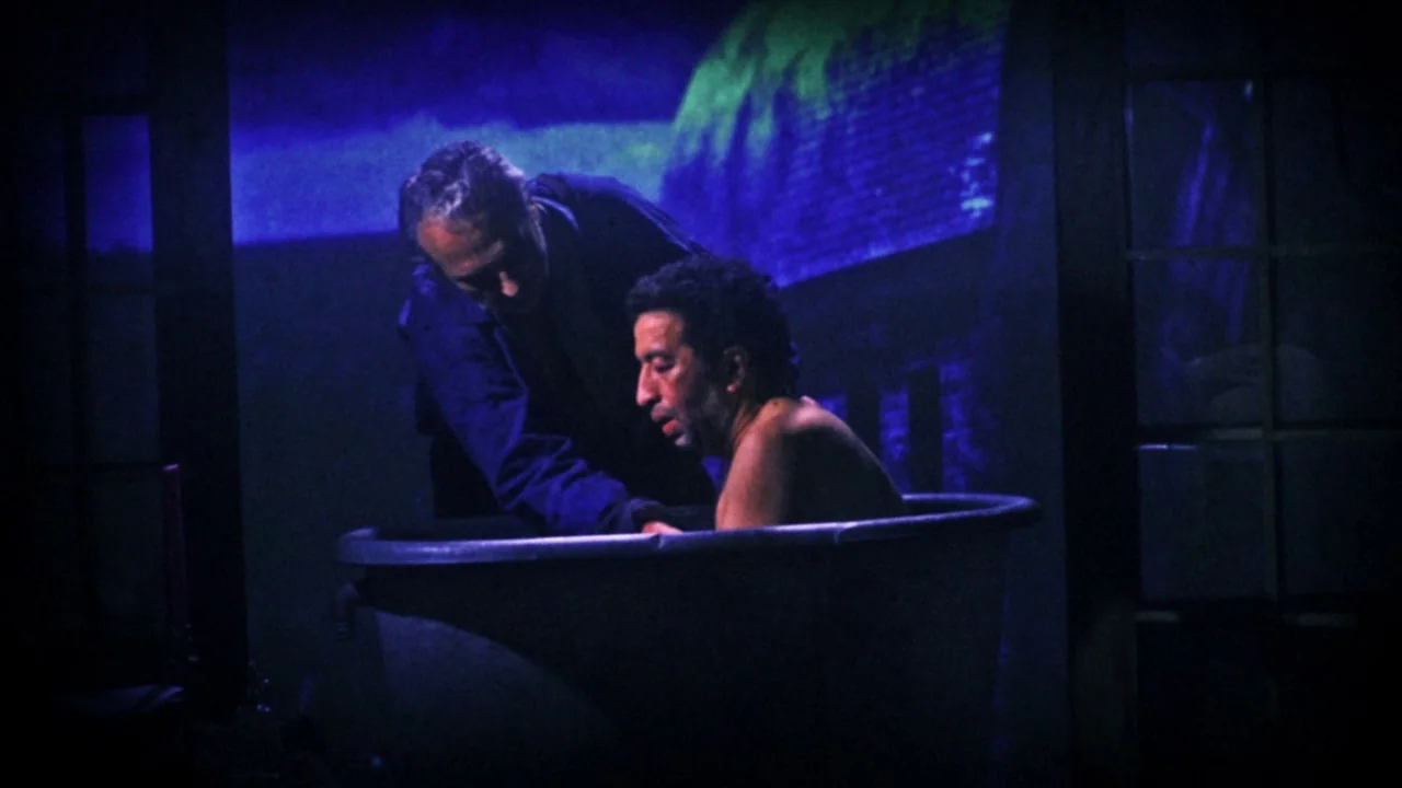 The Forbidden Room (2015) movie still: medium — A dark bathroom is washed in blue light with a deep tub centrally located. A man leans over the tub…