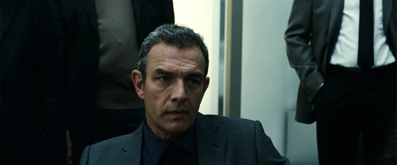 Hereafter (2010) movie still: closeup — An interior space features a man in a formal suit positioned in the foreground. Two other figures in suits…