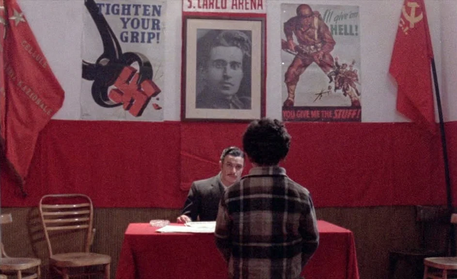 The Kingdom of Naples (1978) movie still: medium — A room with white walls displays communist propaganda posters and a framed portrait above a desk.…