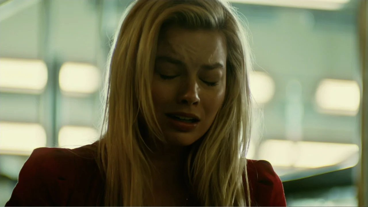 Focus (2015) movie still: closeup — An interior space features bright, blurred rectangular lights against a pale, greenish-toned wall. A woman with…