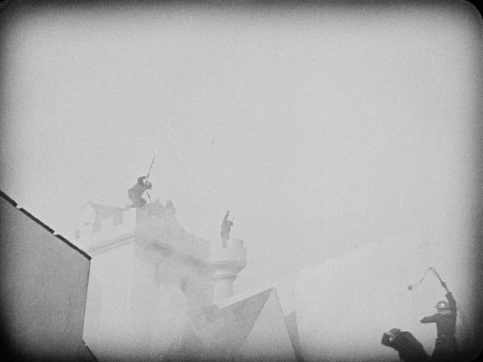 The Passion of Joan of Arc (1928) movie still: wide — A stone fortress wall stands against an empty, bright, hazy sky. Soldiers move along the…
