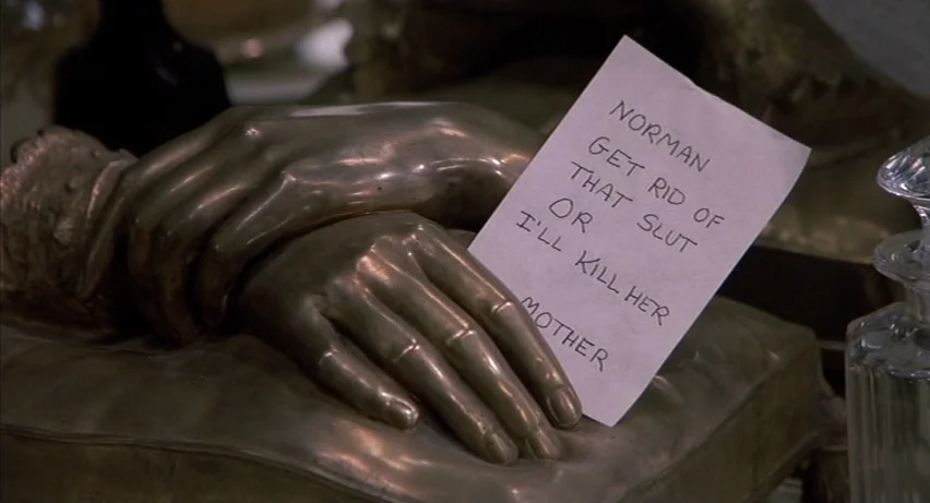 Psycho 2 (1983) movie still: closeup — A bronze sculpture of joined hands sits on a flat surface next to paper. A note with handwritten black ink…