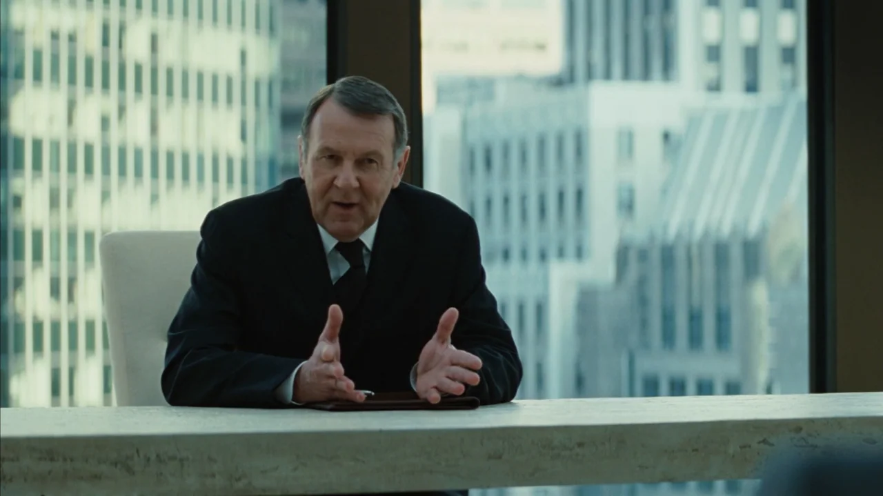 Duplicity (2009) movie still: medium — A high-rise executive office features a view of tall city buildings through large windows. An older man in a…
