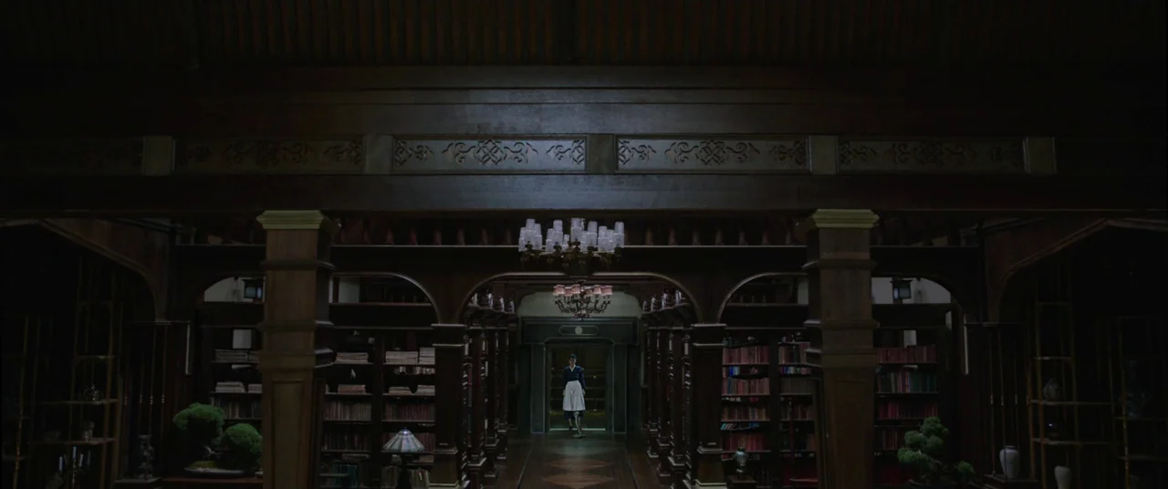 The Handmaiden (2016) movie still: wide — A dark, expansive room with dark wood shelving and multiple archways. A lone woman stands in a distant…