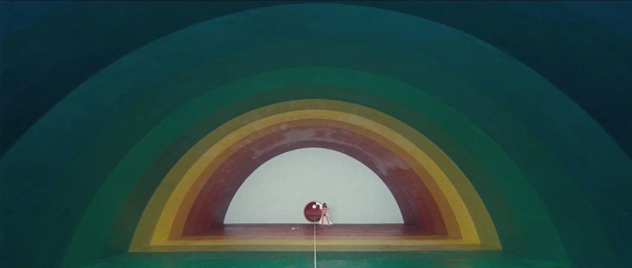 The Holy Mountain (1973) movie still: wide — A large, multi-colored rainbow-painted archway frames a white circular room at the end. A small lone…