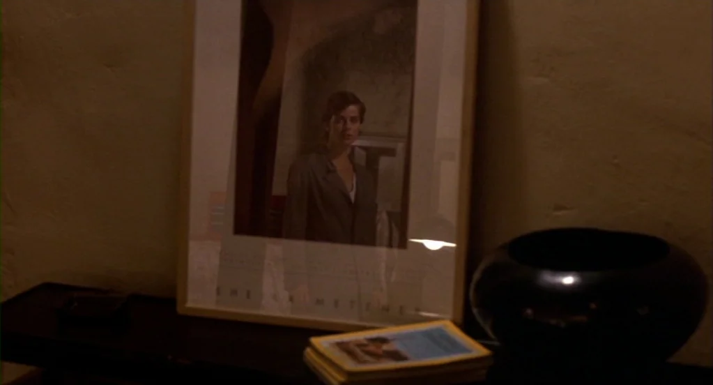 Cat People (1982) movie still: closeup — A framed photograph sits on a dark surface next to a decorative ceramic bowl. The portrait shows a woman in…