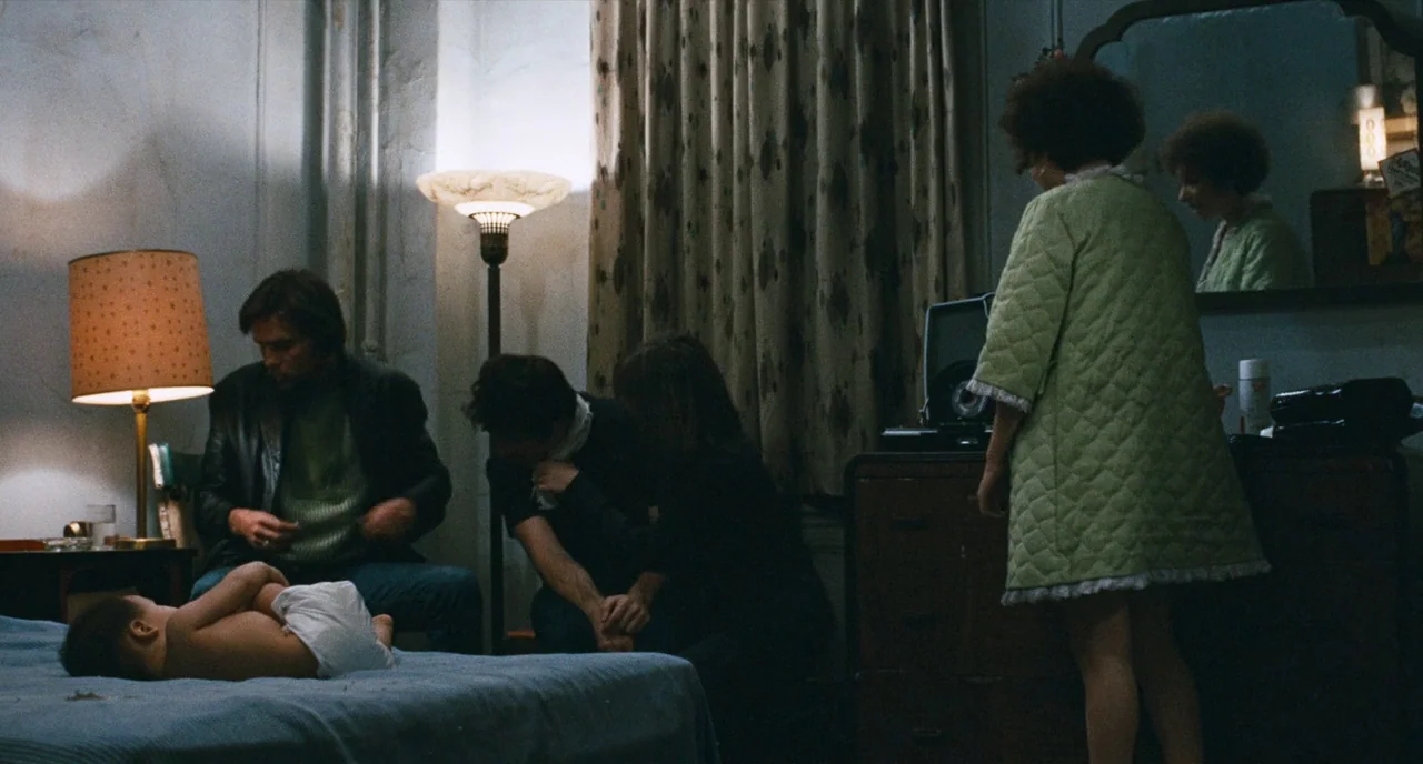 The Panic in Needle Park (1971) movie still: wide — A dimly lit room with heavy curtains and dated furniture contains several seated adults. An…