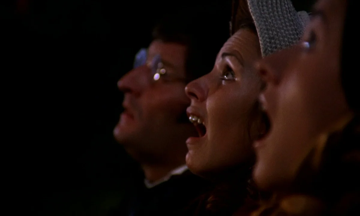 Vampire Circus (1972) movie still: closeup — A dark indoor space where several people sit together in rows. They look upward with open mouths toward…