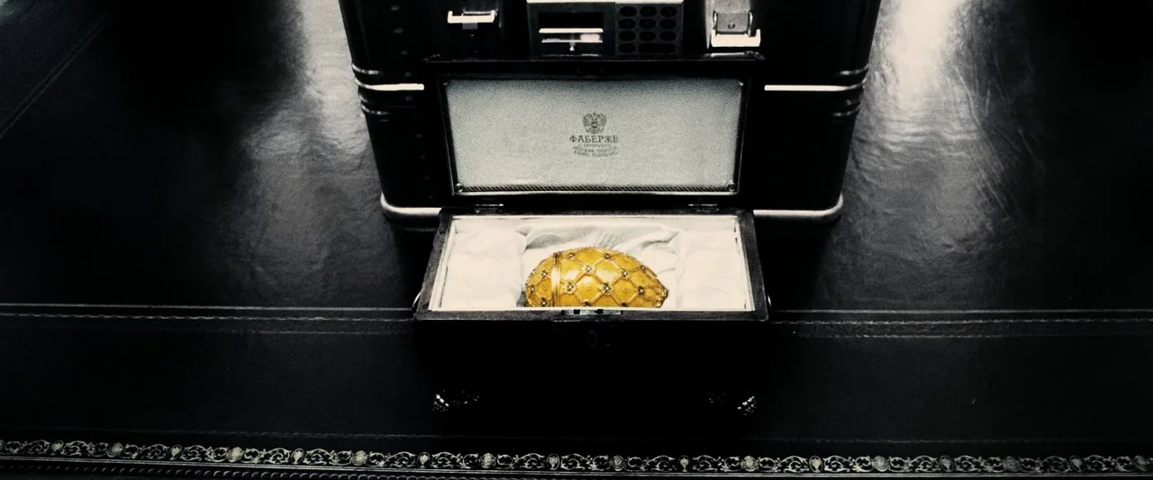 Ocean’s Twelve (2004) movie still: closeup — A high-angle view displays a golden, jeweled egg inside an open black display box. The box lid features…