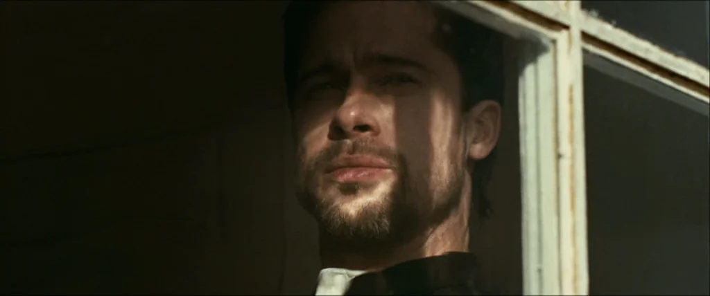 The Assassination Of Jesse James By The Coward Robert Ford (2007) movie still: closeup — A man stands near a window frame with light casting…