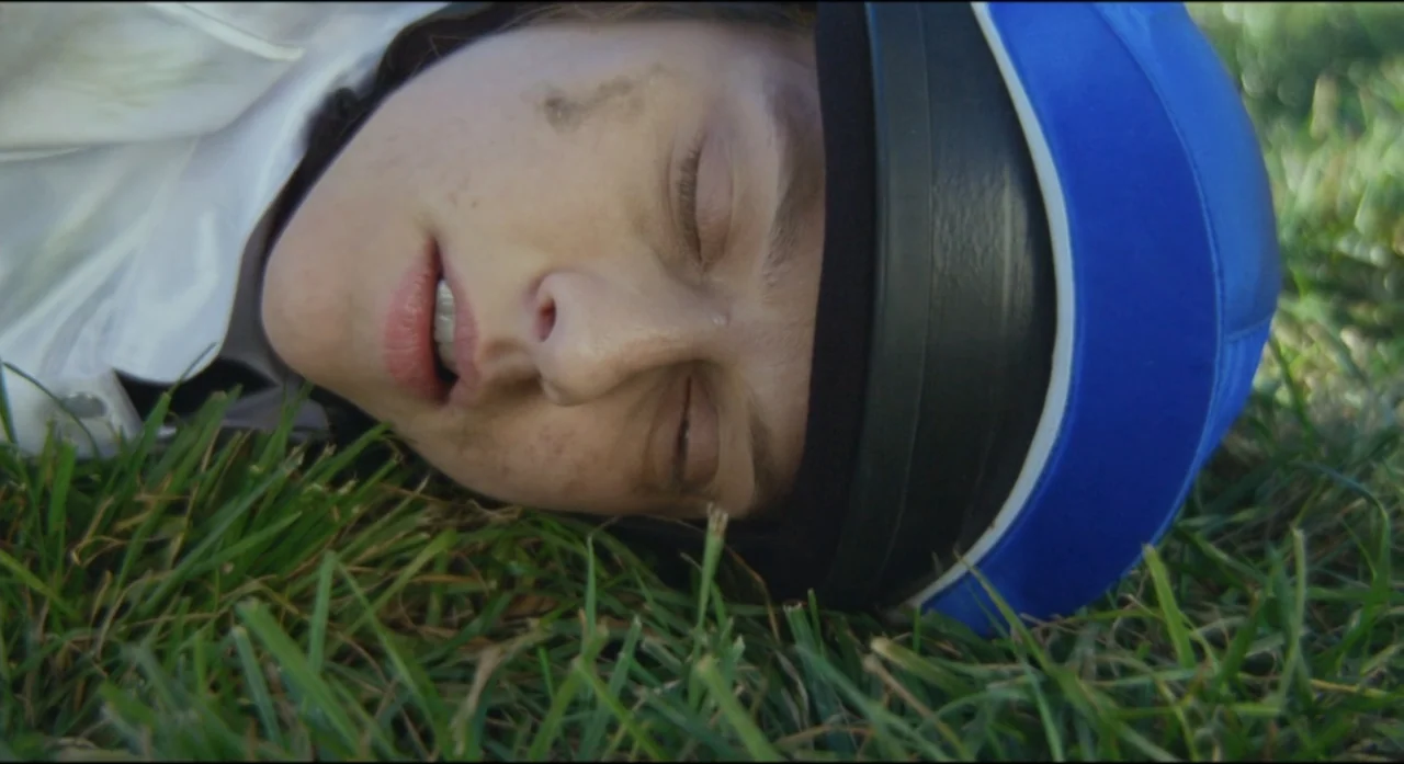 Ride Like a Girl (2019) movie still: closeup — A person lies still on a patch of green grass in an open field. The individual wears an equestrian…