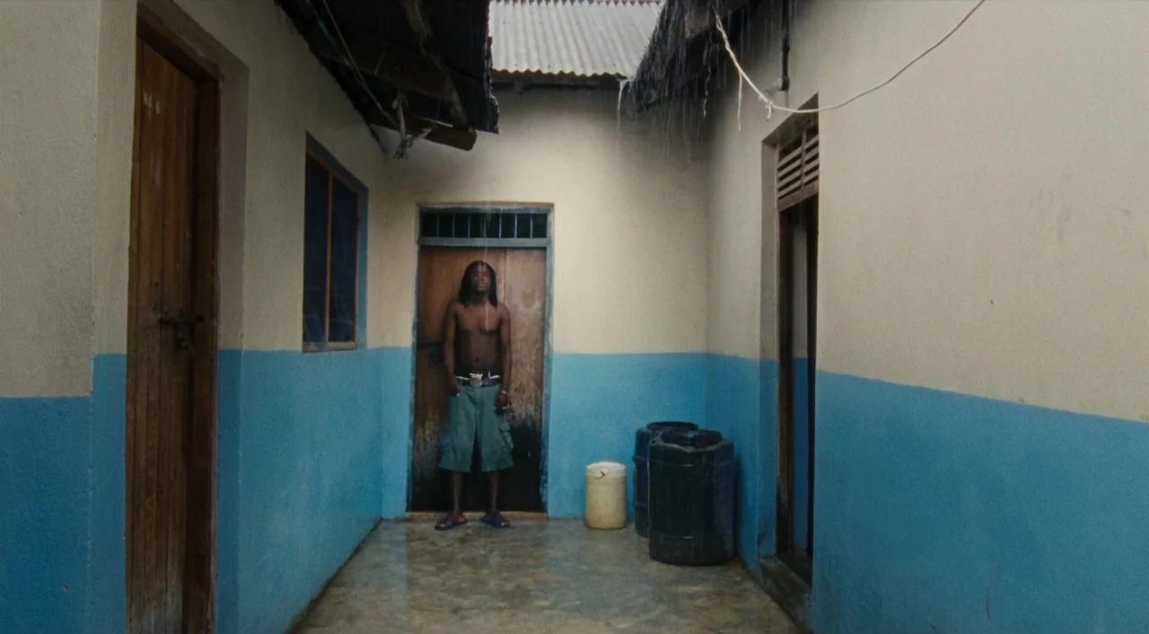 Paradise: Love (2012) movie still: fullbody — A narrow outdoor corridor features white and blue painted walls with corrugated metal roofing. A…