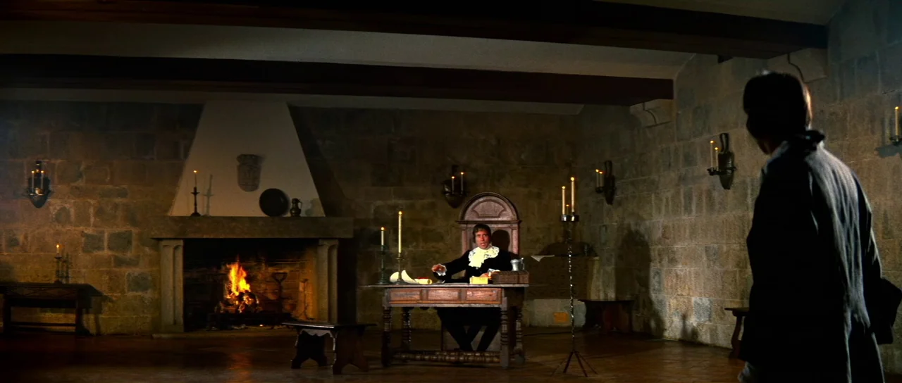 Night of the Blood Monster (1970) movie still: wide — A spacious stone chamber features a large hearth and medieval-style furnishings. A man sits at…