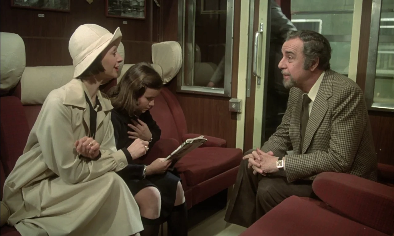 That Obscure Object of Desire (1977) movie still: medium — A vintage railway cabin features dark wood paneling and burgundy plush seats. A woman in…